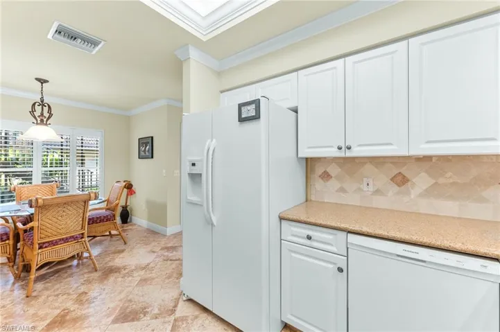 Kitchen with ornamental molding, white appliances, light stone counters, hanging light fixtures, and white cabinetry