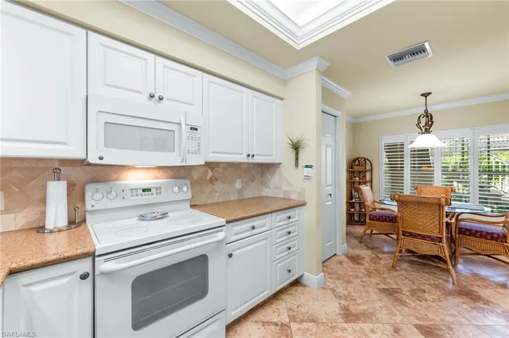 Kitchen featuring white appliances, ornamental molding, light stone counters, decorative light fixtures, and white cabinetry