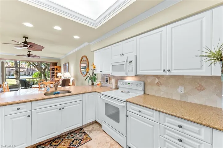 Kitchen with white appliances, white cabinets, ceiling fan, recessed lighting, and light stone counters