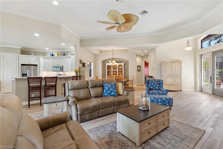 Living room featuring a tray ceiling, ornamental molding, ceiling fan with notable chandelier, and light hardwood / wood-style flooring