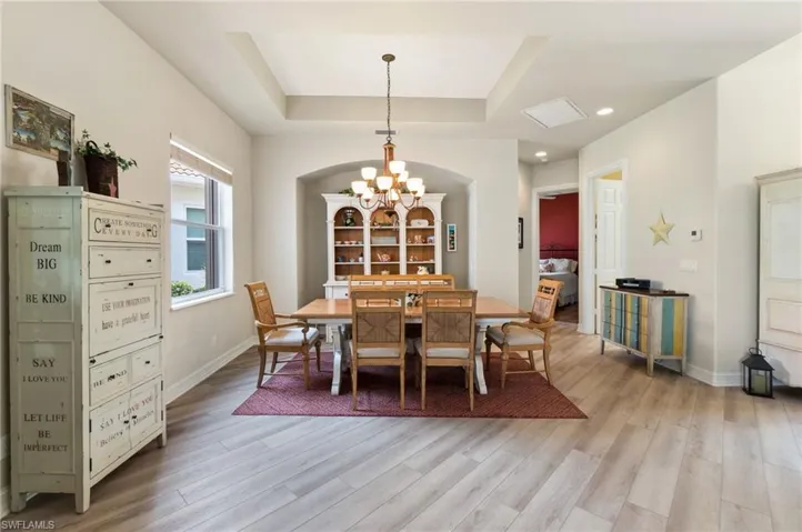 Dining room with a notable chandelier, light wood-type flooring, and a raised ceiling