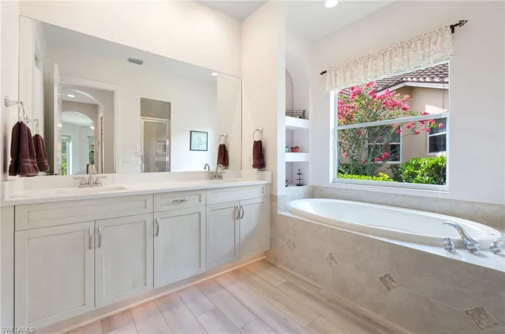 Bathroom with double sink, wood-type flooring, oversized vanity, and tiled tub