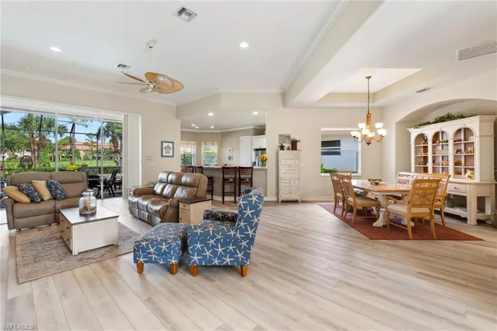 Living room featuring ceiling fan with notable chandelier, a raised ceiling, light hardwood / wood-style flooring, and crown molding
