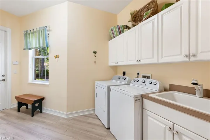 Clothes washing area featuring light hardwood / wood-style floors, washing machine and clothes dryer, electric dryer hookup, sink, and cabinets