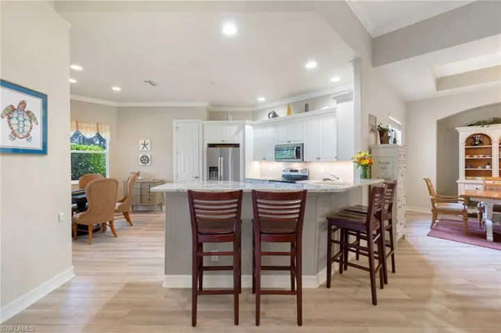 Kitchen with crown molding, stainless steel appliances, light stone counters, a breakfast bar area, and white cabinetry