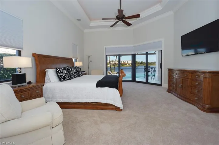 Bedroom with light carpet, access to outside, a high ceiling, a raised ceiling, and ceiling fan