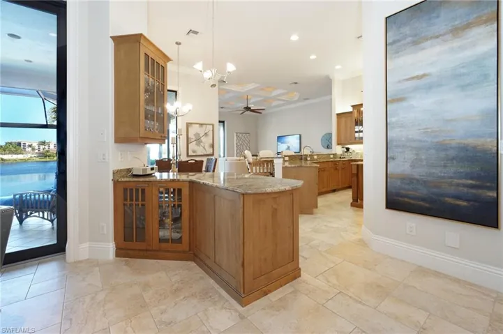 Kitchen with pendant lighting, coffered ceiling, light stone countertops, ornamental molding, and kitchen peninsula