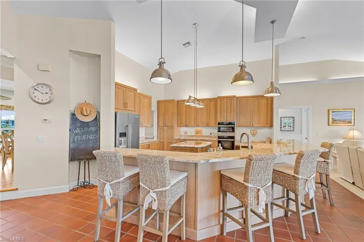 Kitchen featuring high end refrigerator, decorative light fixtures, high vaulted ceiling, and a kitchen breakfast bar
