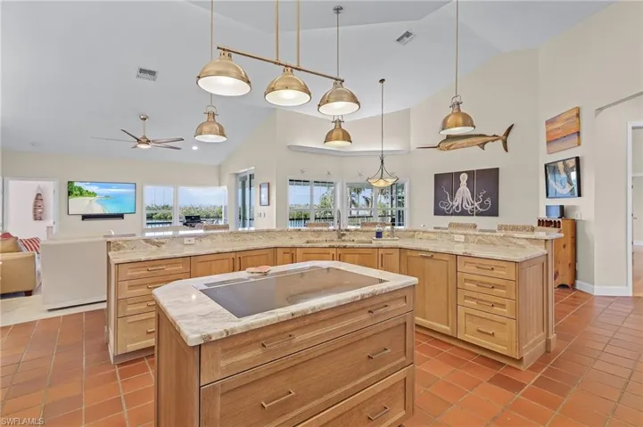 Kitchen with ceiling fan, hanging light fixtures, cooktop, tile patterned flooring, and a spacious island