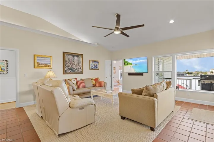 Living room with light tile patterned floors, ceiling fan, and lofted ceiling