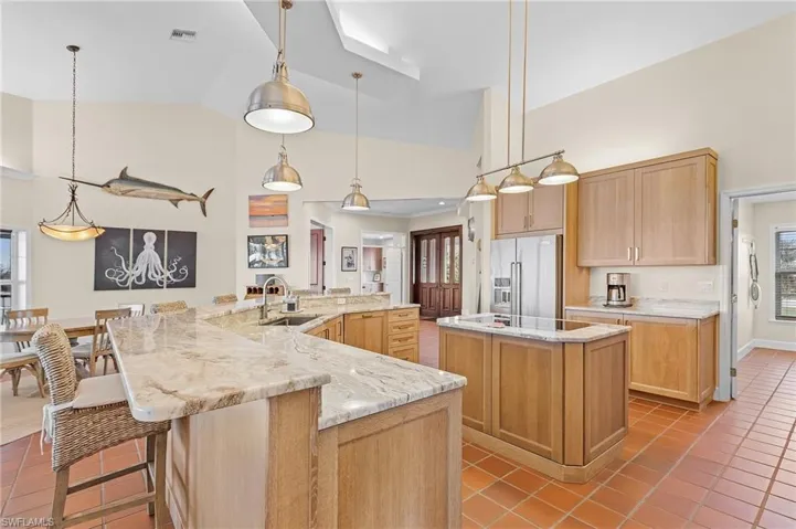 Kitchen with light tile patterned flooring, a spacious island, sink, hanging light fixtures, and high end fridge