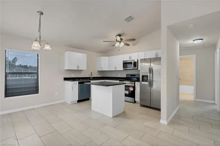 Kitchen featuring hanging light fixtures, white cabinetry, a center island, appliances with stainless steel finishes, and lofted ceiling