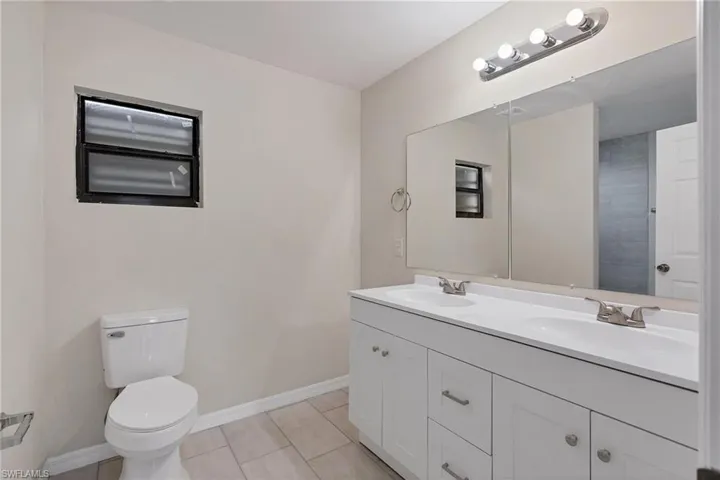 Bathroom with double vanity, tile flooring, and toilet