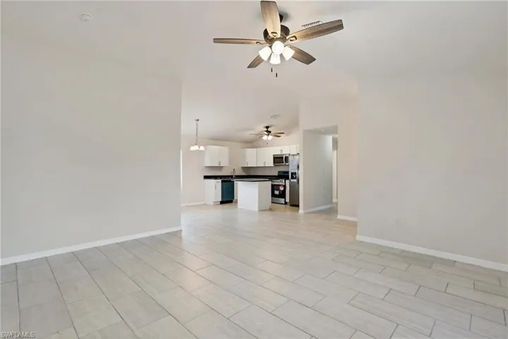 Unfurnished living room with sink, ceiling fan, and light tile floors