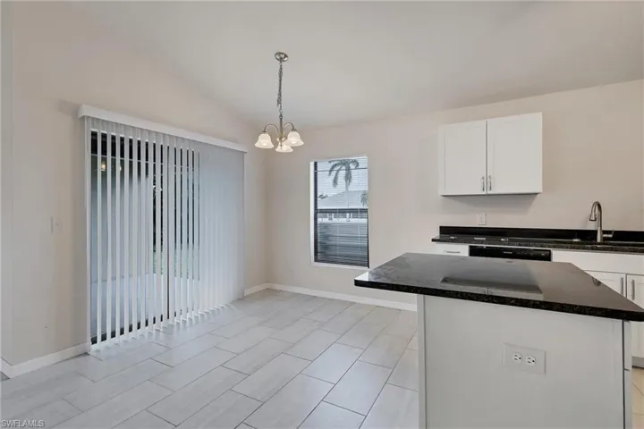 Kitchen featuring an inviting chandelier, hanging light fixtures, white cabinets, sink, and lofted ceiling