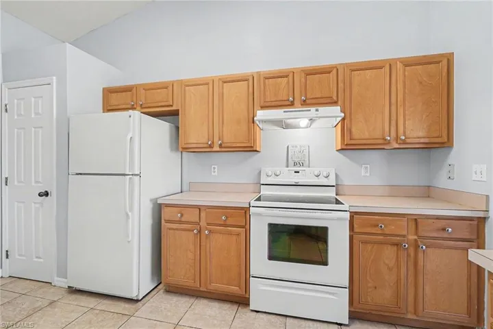 Kitchen featuring white appliances, light countertops, light tile patterned floors, and wood finish cabinets