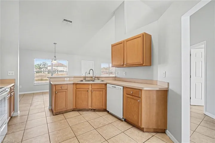 Kitchen with light countertops, a peninsula, light tile patterned floors, white appliances, and lofted ceiling