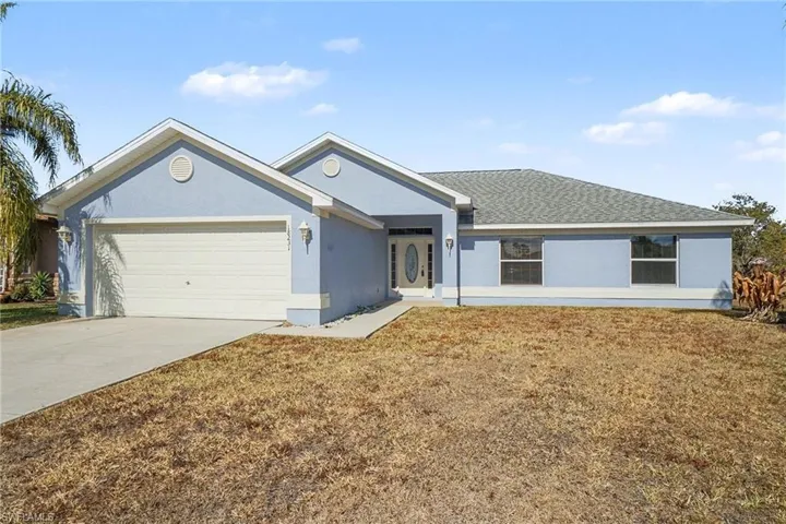 Ranch-style home with stucco siding, driveway, a garage, a shingled roof, and a front yard