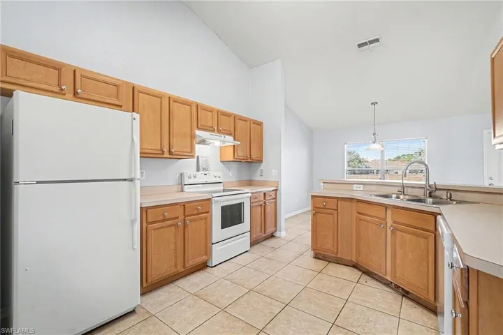 Kitchen featuring white appliances, lofted ceiling, light countertops, a peninsula, and pendant lighting