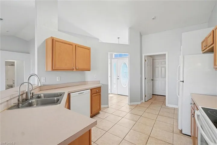 Kitchen featuring light countertops, white appliances, a peninsula, light tile patterned flooring, and vaulted ceiling