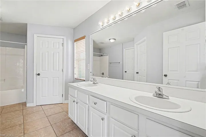 Bathroom with double vanity, light tile patterned floors, and washtub / shower combination