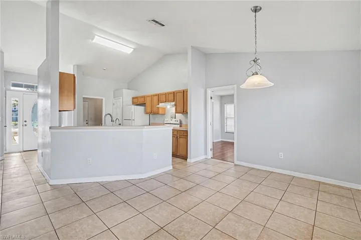Kitchen featuring wood finish cabinets, lofted ceiling, hanging light fixtures, freestanding refrigerator, and light countertops