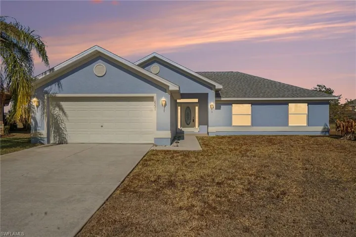 Ranch-style house with concrete driveway, a garage, a lawn, stucco siding, and roof with shingles