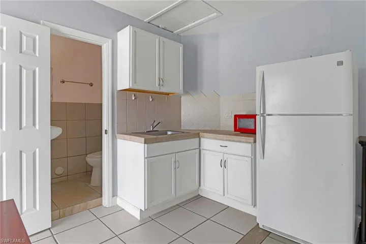 Kitchen with sink, white cabinets, white fridge, and light tile floors