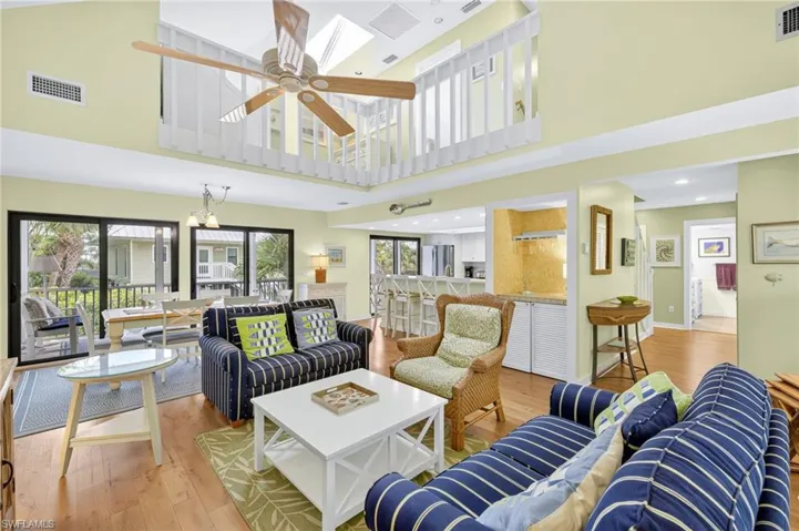 Living area with a towering ceiling, healthy amount of natural light, wood finished floors, a ceiling fan, and recessed lighting