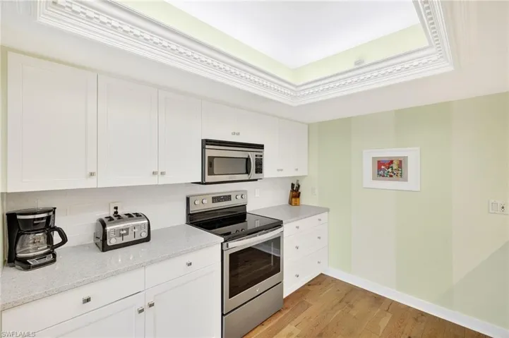 Kitchen featuring stainless steel appliances, tasteful backsplash, light wood finished floors, white cabinetry, and light stone counters