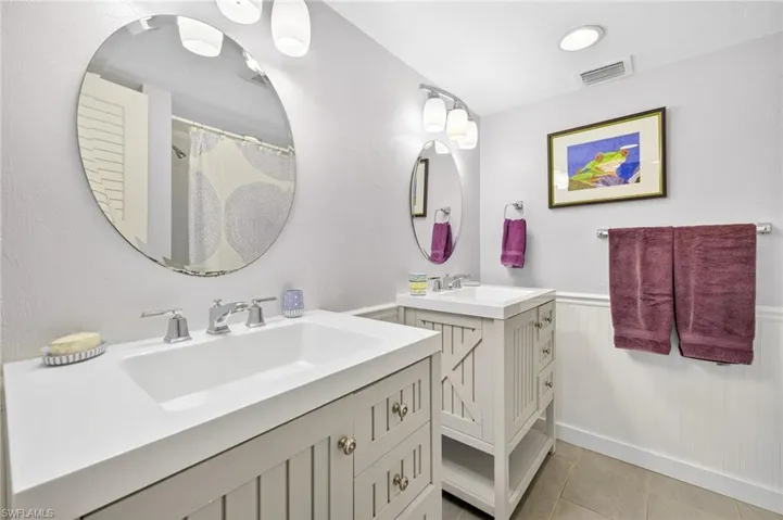 Full bath featuring two vanities, tile patterned floors, and wainscoting