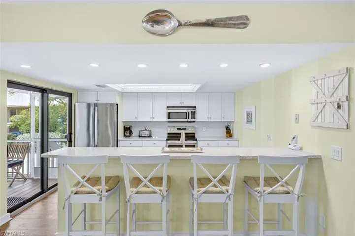 Kitchen featuring stainless steel appliances, a kitchen bar, light countertops, recessed lighting, and backsplash