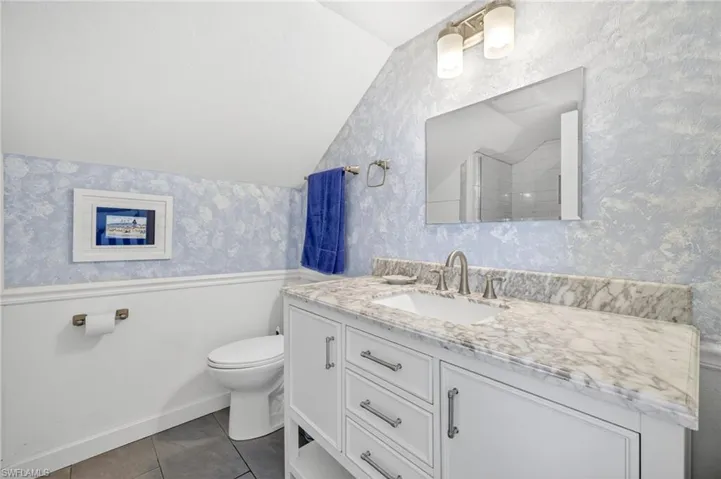 Full bathroom featuring vaulted ceiling, vanity, tile patterned floors, wallpapered walls, and a wainscoted wall