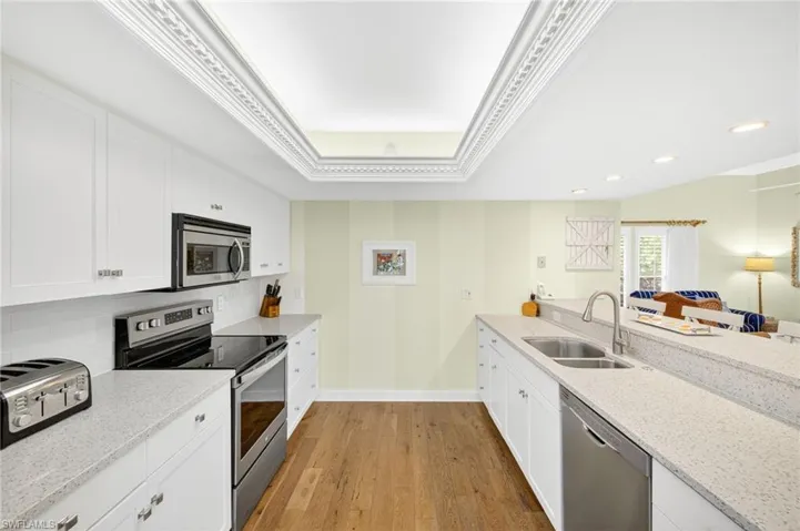 Kitchen with stainless steel appliances, light stone countertops, backsplash, light wood-style flooring, and a tray ceiling