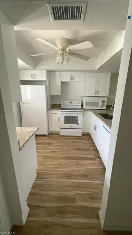Kitchen with white cabinets, white appliances, light wood-style flooring