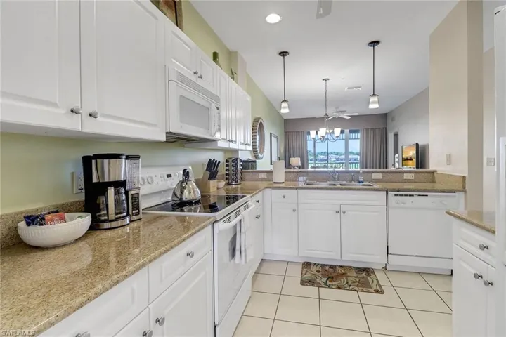 Kitchen with white cabinets, hanging light fixtures, and white appliances