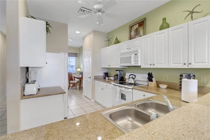 Kitchen with white cabinetry, sink, ceiling fan, white appliances, and light tile patterned floors