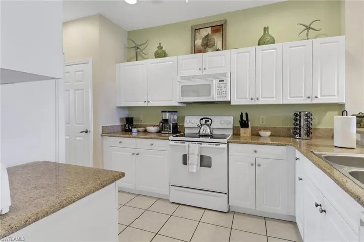 Kitchen with light tile patterned floors, white cabinets, white appliances, and sink