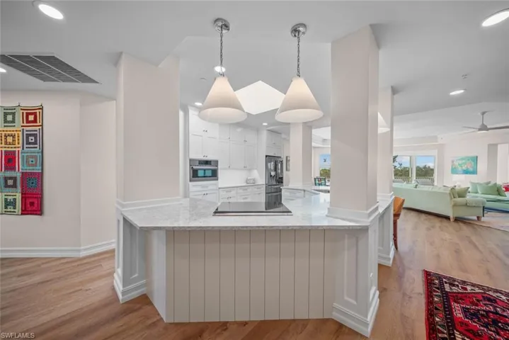 Kitchen with pendant lighting, light hardwood / wood-style flooring, light stone counters, white cabinetry, and stainless steel appliances