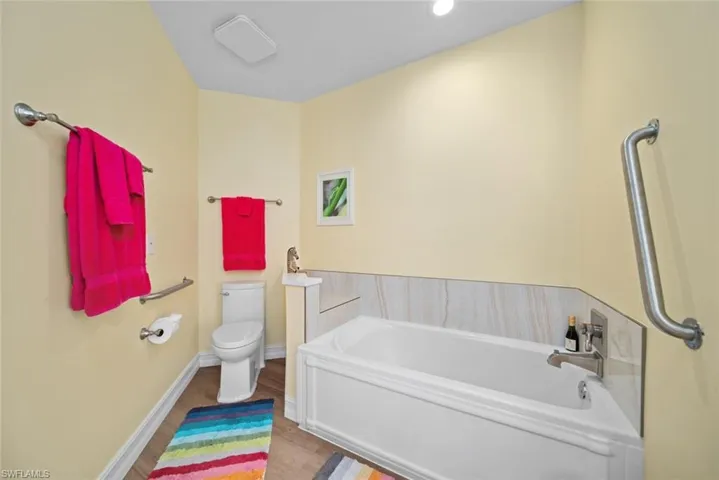 Bathroom featuring hardwood / wood-style flooring, toilet, and a tub to relax in
