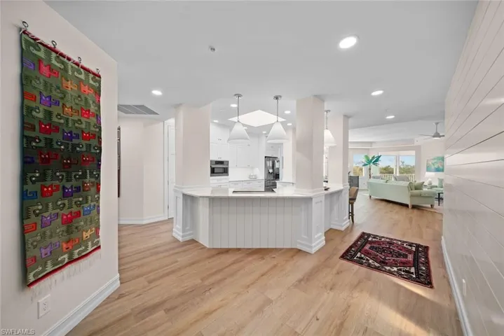 Kitchen featuring kitchen peninsula, pendant lighting, light hardwood / wood-style flooring, white cabinets, and a breakfast bar area