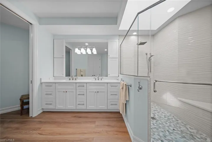Bathroom featuring hardwood / wood-style flooring, vanity, walk in shower, and a skylight