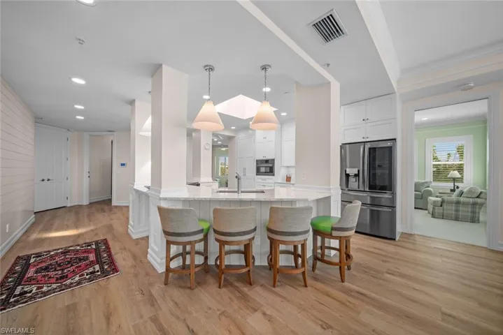 Kitchen featuring pendant lighting, white cabinets, stainless steel refrigerator with ice dispenser, light hardwood / wood-style flooring, and light stone counters