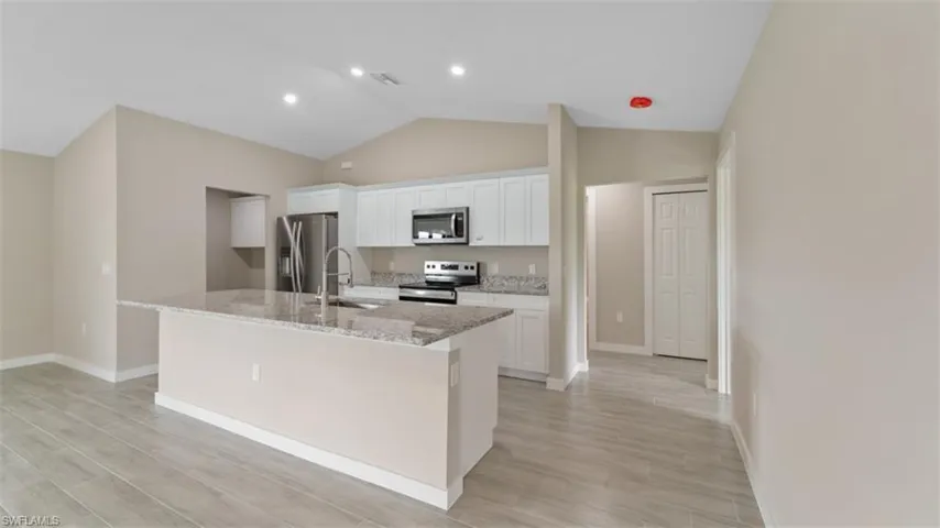 Kitchen featuring appliances with stainless steel finishes, white cabinetry, an island with sink, and light stone countertops