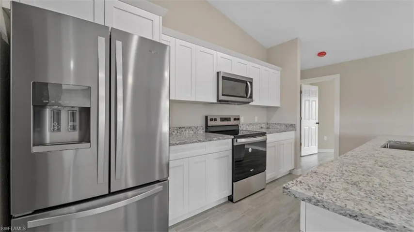 Kitchen featuring lofted ceiling, light stone countertops, appliances with stainless steel finishes, and white cabinets