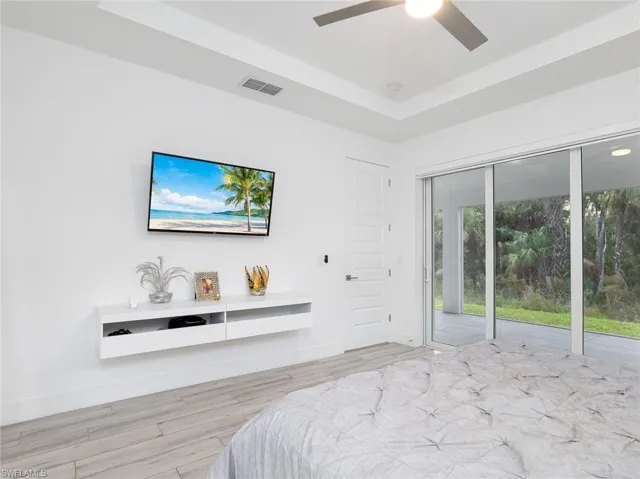 Bedroom featuring visible vents, baseboards, a raised ceiling, ceiling fan, and wood finished floors