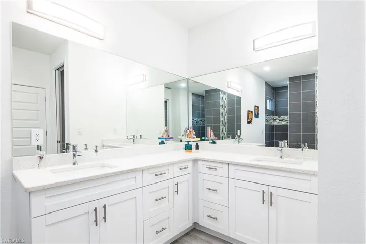 Full bath with double vanity, a tile shower, a sink, and wood finished floors
