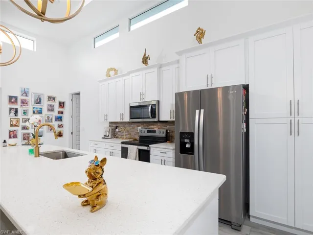Kitchen featuring appliances with stainless steel finishes, light stone counters, white cabinetry, decorative backsplash, and a sink