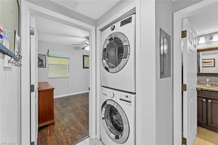 Laundry room featuring ceiling fan, stacked washer and dryer, hardwood / wood-style floors, and electric panel