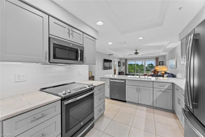 Kitchen featuring appliances with stainless steel finishes, ceiling fan, a raised ceiling, and gray cabinetry